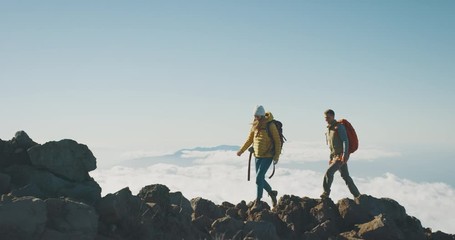 young adventurous backpackers hiking to the top of a mountain above the clouds, happy couple hiking 