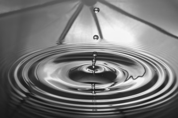 Water droplets falling against the surface of the water create a beautiful ripple on the gray water surface.