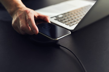 Wall Mural - man charging mobile phone on wireless charger on table