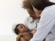 Asian Doctor Checking On African Baby Boy In Mother's Arms. Healthcare For Baby Concept.