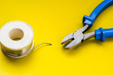 Wall Mural - Diagonal cutting nippers and solder on a yellow background. Nippers with blue handles a solder coil. Jack of all trades or industry. Close-up. Selective focus. Shooting from above at an angle.