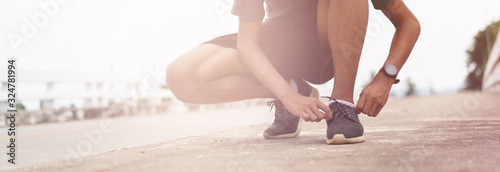 Fotomural Tie a shoe,Asian male jogger athlete training and doing workout outdoors on a street, He tying laces for jogging on road with running shoes