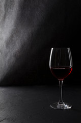 One glass of red wine on the black table against dark wall.Vertical image