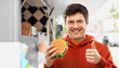 © Syda Productions - fast food, takeaway and people concept - happy smiling young man in red hoodie with hamburger showing thumbs up over food truck on street background