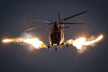 Military Helicopter In Flight Firing Off Flare Decoys At Night.