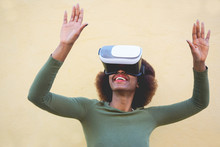 Young Woman Using Virtual Reality Headset With Yellow Wall In Background - African Woman Having Fun With New Trend Technology - Tech, Fun And Future Concept - Focus On Girl Mouth And Vr Glasses