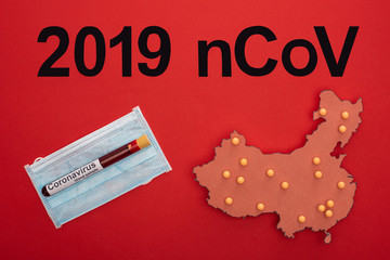 Wall Mural - Top view of 2019 ncov lettering, layout of china map with test tube on medical mask on red surface