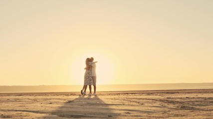 Wall Mural - A beautiful romantic couple man and woman are hugging on the sunny beach near the lake against the sunrise