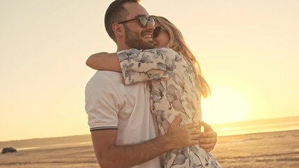 Poster - A good-looking smiling young couple man and woman wearing sunglasses are hugging on the sunny beach near the lake