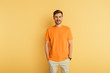 © LIGHTFIELD STUDIOS - smiling young man in orange t-shirt standing with hands in pockets on yellow background
