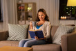 © Syda Productions - leisure, literature and people concept - young woman reading book at home in evening