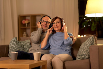 Wall Mural - technology, old age and people concept - happy senior couple with headphones listening to music at home in evening