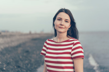 Authentic portrait of a brunette woman in a striped casual dress by the sea.