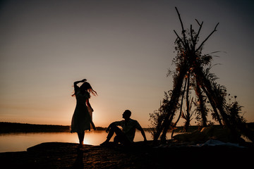 Young couple is embracing in the water on Sunset. Two silhouettes against the sun. Romantic love story. Wigwam on the stone.