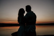 © malysheva - Young couple is embracing on the sunset coast. Two silhouettes against the sun. Romantic love story.