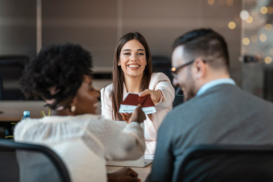 The travel agent keeps tickets for the plane in the travel agency. She offers them to clients. She smiles. Photo of female travel agent. Young woman smiling, proposing tourist tickets. 