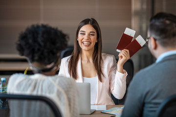 Wall Mural - The travel agent keeps tickets for the plane in the travel agency. She offers them to clients. She smiles. Photo of female travel agent. Young woman smiling, proposing tourist tickets. 