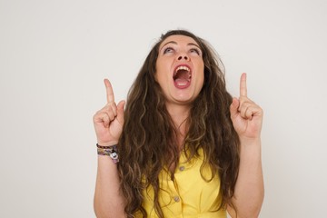 Charming carefree woman with positive expression, points up with both index fingers, dressed in casual clothing, has broad interested smile, isolated over gray background. Look there, please.