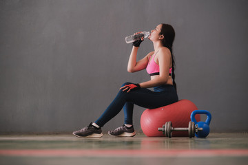 Sporty young women sitting on gymnastic ball and drinking water after work out