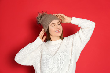 Canvas Print - Young woman wearing warm sweater and hat on red background. Winter season