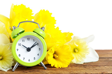 Poster - Green alarm clock and spring flowers on wooden table against white background. Time change