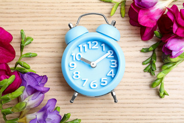 Poster - Light blue alarm clock and spring flowers on wooden table, flat lay. Time change
