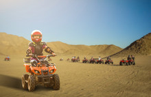 Little Girl Riding ATV Quad Bike In Desert With Beautiful Blue And White Sky .