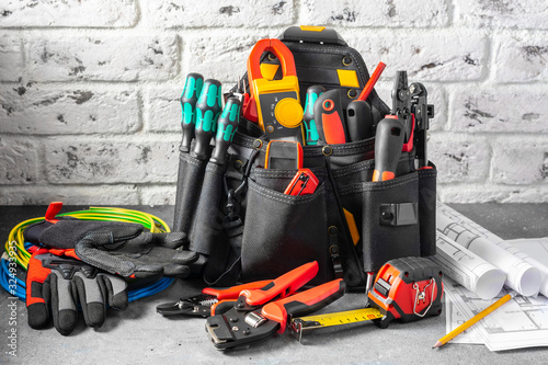 Electrician\'s tools in a black construction bag on a gray table against a white brick wall. Construction tools of an installer or electrician. Space for text