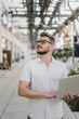 © Westend61 - Young man holding laptop and looking up in the city
