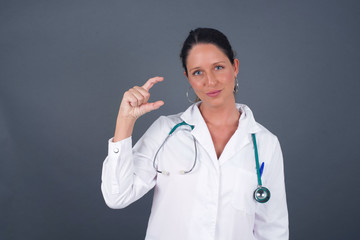 European doctor woman over isolated background gesturing with hand showing small size, measure symbol. Smiling looking at the camera. Measuring concept.