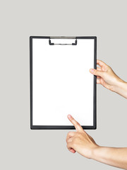 Wall Mural - clipboard in female hands. hand holds a clipboard with a white sheet of paper and points at empty space on a gray isolated background. mockup, template for text