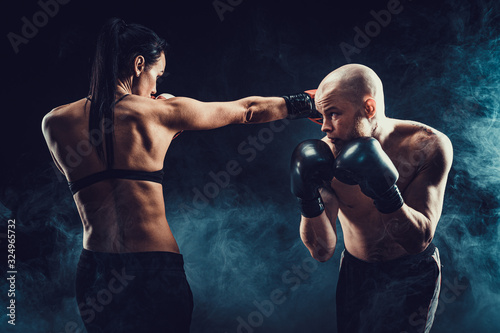 Fotografía Shirtless Woman exercising with trainer at boxing and self defense lesson, studio, dark background