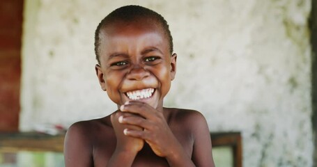authentic portrait of happy rural african boy is smiling in camera on a village background. concept: