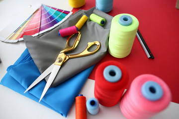 Fashion Designing Tailor Craftsmanship Concept. Fabric, Color Palette and Sewing Tools on Table. Needle Machine Bobbins Spools of Thread with Gold Scissors on Silk Piece. Designer Working Desk