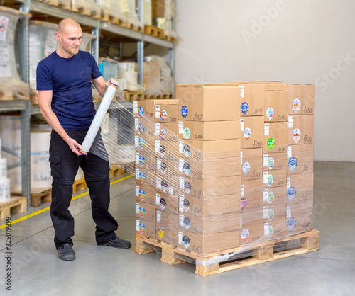 Fotografía Man wrapping (stretching) of a loaded pallet with foil - most common and fastest way to stabilize the goods on the pallet