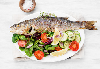 Wall Mural - White plate of baked sea bass with fresh green salad.