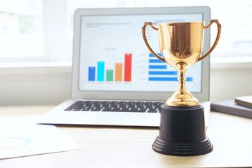 Wall Mural - gold trophy with background laptop computer on the working table near the window.