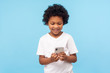 © khosrork - Happy adorable excited little boy with curly hair reading funny message on smartphone and smiling, satisfied with children mobile application, using cellphone. studio shot isolated on blue background