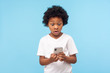 © khosrork - Astonished cute little boy with curly hair reading message on smartphone and expressing amazement shock, surprised by mobile application, using cellphone. studio shot isolated on blue background