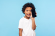 © khosrork - Excited funny adorable little boy with curly hair holding cellphone near face, child satisfied rejoicing new mobile phone and looking with pleased smile. indoor studio shot isolated on blue background