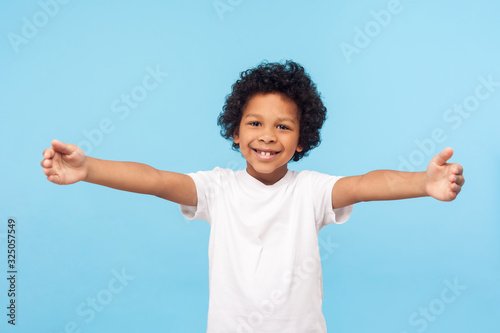 Photographie Come here, free hugs! Portrait of lovely good-natured little boy with curly hair in white T-shirt smiling excitedly and holding hands wide open to embrace, greeting