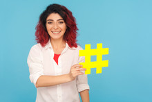 Blogs And Popular Topics. Charming Happy Woman With Fancy Red Hair Holding Big Hashtag Symbol And Smiling To Camera, Hash Sign To Tag Forum Discussions. Indoor Studio Shot Isolated On Blue Background