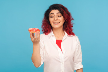 Sweet temptation. Portrait of hungry pretty woman looking at appetizing donut with desire, craving to bite delicious pastry, high-calorie junk food. indoor studio shot isolated on blue background