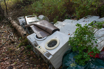 Old obsolete household washing machines and other trash dumped illegally in forest.