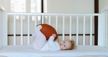 Caucasian Baby Playing With American Football Ball In Bed. RAW Graded Footage 4K Slow Motion 50fps