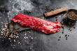 Raw skirt, machete steak on a meat cleaver. Black background. Top view