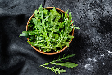 Poster - Fresh rucola in a wooden bowl. Black background. Top view