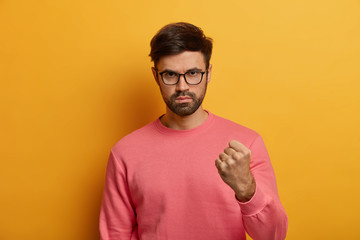 serious irritated aggressive man holds fist up, expresses negative feelings and attitude, threatenin