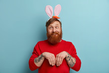 Funny Ginger Man Pretends Being Easter Bunny, Goes Crazy, Crosses Eyes, Keeps Palms Like Rabbit, Wears Fluffy Ears, Red Jumper, Celebrates Spring Holidays, Has Funny Expression, Poses Over Blue Wall.