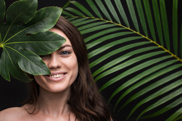 Portrait of a young beautiful woman with tropical leaf on black background. Female perfect smooth skin. Organic, natural cosmetics, skin care, health, ecology, nature, spa, wellness.